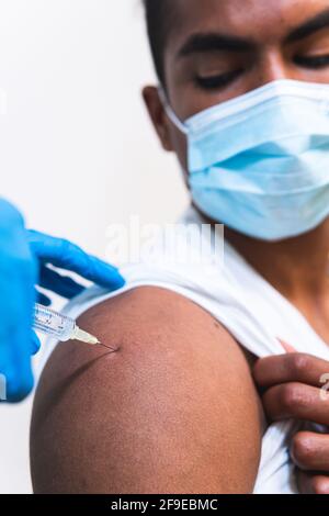 Kurzgeschnittene, nicht erkennbare Ärztin in Schutzkleidung, Latexhandschuhen und Gesichtsmaske zur Impfung afroamerikanischer männlicher Patienten in der Klinik Stockfoto