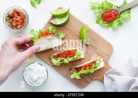 Kleine leckere Tacos mit rotem Kaviar und grünem Salat serviert Auf Holzschneidebrett auf Tisch Stockfoto