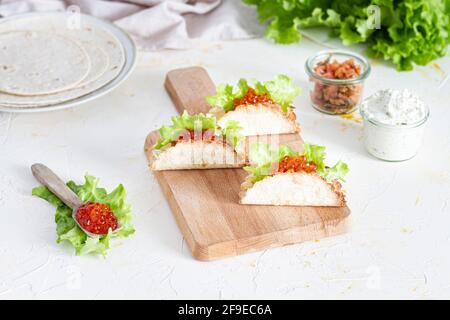 Kleine leckere Tacos mit rotem Kaviar und grünem Salat serviert Auf Holzschneidebrett auf Tisch Stockfoto