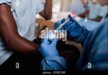 Crop Hände von anonymen Arzt in Latexhandschuhe füllen Spritze aus der Flasche mit Impfstoff, der die Impfung von nicht erkennbaren Männern vorbereitet Afroamerikanisch Stockfoto