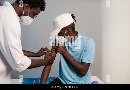 Seite schwarz Arzt in Schutzuniform und Latexhandschuhe impfen Afroamerikanischer Patient in der Klinik während des Coronavirus-Ausbruchs Stockfoto