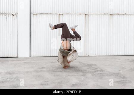 Nicht erkennbarer männlicher Tänzer, der Breakdance-Bewegungen zeigt, während er auf den Armen balanciert Und die Durchführung von Handhopps auf Betonboden im Stadtgebiet Stockfoto