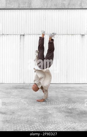 Nicht erkennbarer männlicher Tänzer, der Breakdance-Bewegungen zeigt, während er auf den Armen balanciert Und die Durchführung von Handhopps auf Betonboden im Stadtgebiet Stockfoto