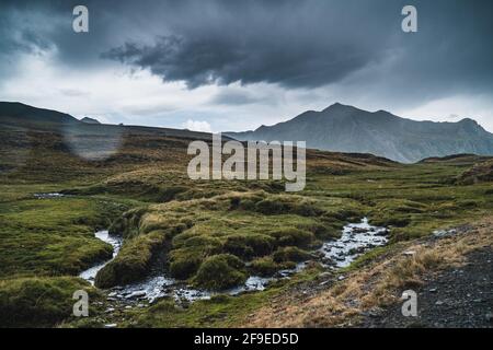 Atemberaubende Landschaft von Wiese mit grünem Gras und Bach fließt Auf den Hügeln unter dem trüben Himmel in den Pyrenäen in Spanien Stockfoto