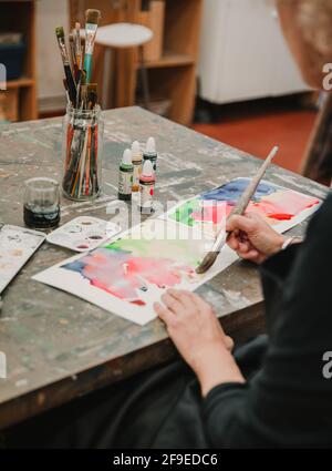Schneiden Sie unkenntlich weibliche Künstler Malerei mit Aquarellen auf Papier, während Sitzen am Tisch im Kunststudio Stockfoto