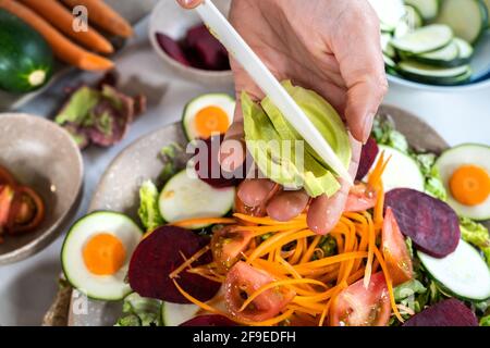 Von oben der Ernte unkenntlich Person Schneiden reife Avocado während Vegetarische Gerichte mit verschiedenen Gemüsesorten zubereiten Stockfoto