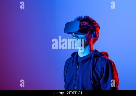 Nicht erkennbarer bärtiger Mann im Headset, der die virtuelle Realität in Neon erforscht Leicht Stockfoto