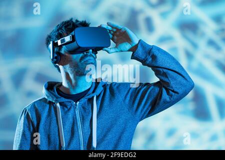 Nicht erkennbarer bärtiger Mann im Kapuzenpullover und modernem Headset, der virtuelle Welt erkundet Realität im Neonlicht Stockfoto