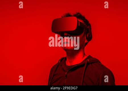Nicht erkennbarer bärtiger Mann im Kapuzenpullover und modernem Headset, der virtuelle Welt erkundet Realität im Neonlicht Stockfoto