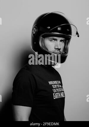 Seitenansicht eines selbstbewussten, brutalen erwachsenen Mannes in einem schwarzen Motorrad Der Helm blickt auf die Kamera, während er vor dem Hintergrund des Studios steht Stockfoto