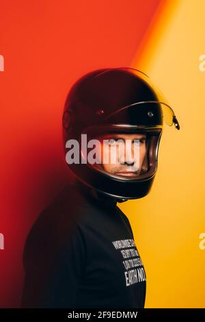 Seitenansicht eines selbstbewussten, brutalen erwachsenen Mannes in einem schwarzen Motorrad Helm blickt auf die Kamera, während er gegen das bunte Rot und steht Gelber Hintergrund Stockfoto