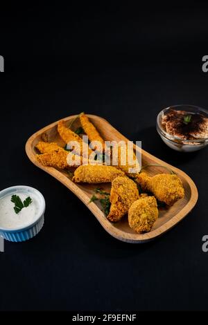Eine vertikale Aufnahme einer Portion knuspriger Hähnchenflügel Und Nuggets mit Saucen auf schwarzem Hintergrund Stockfoto