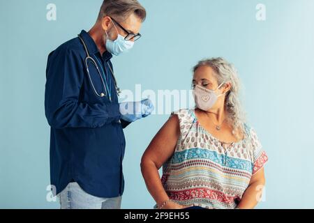 Männlicher Arzt bereitet Spritze für die Impfung älterer Frau vor blauem Hintergrund vor. Arzt und ältere Frau mit Gesichtsmasken während des Covid-19-Impfens Stockfoto