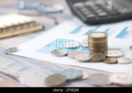 Stapel von Münzen, Finanzgraph, Rechner und Notizblock auf dem Tisch Stockfoto