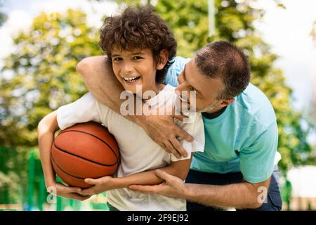 Sportlicher Vater lehrt seinem Sohn, wie man draußen Basketball spielt Stockfoto