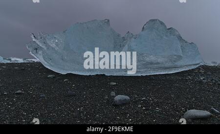 Bizarr aussehender kleiner Eisberg mit klarer Oberfläche am Ufer des berühmten Diamond Beach in der Nähe der Ringstraße an der Gletscherlagune Jökulsárlón im Süden Islands. Stockfoto