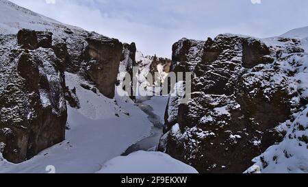 Schöne Aussicht auf die berühmte Schlucht Fjaðrárgljúfur im Süden Islands in der Nähe der Ringstraße mit schneebedeckten Felsen, steilen Klippen und gewundenem Fluss Fjaðrá. Stockfoto