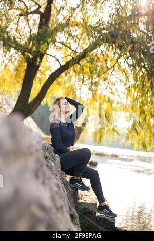 Die Seitenansicht einer blonden, schönen Frau, die darauf sitzt Die Treppe im Wald am See Stockfoto