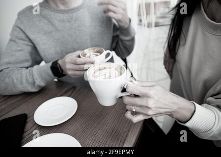 Junges Paar trinkt heiße Getränke. Nahaufnahme Frau und Mann sitzen im Café und halten warme Tassen Kaffee auf dem Tisch. Mann und Frau verbringen Wochenende in Stockfoto
