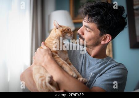 Junger Mann und brauner Tabby-Katze riechen sich gegenseitig. Nahaufnahme Stockfoto