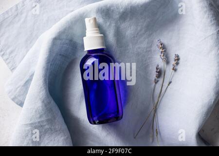 Lavendelspray in blauer Glasflasche auf Leinentuch Stockfoto