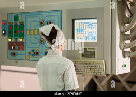 Rückansicht einer Arbeitnehmerin am Bedienfeld der Maschine im Fertigungswerk. Stockfoto