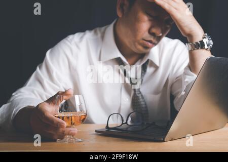 Geschäftsmann hält Whiskey-Glas und fühlt sich gestresst, weil er aufgrund der schlechten wirtschaftlichen Bedingungen im Jahr 2021 als Folge des Covid-19-Ausbruchs hart arbeitet. Stockfoto