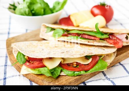 Piadina Romagnola mit Mozzarella-Käse, Tomaten, Schinken und Rucola-Salat auf einem Schneidebrett. Italienisches Fladenbrot oder offenes Sandwich. Selektiver Fokus. Stockfoto