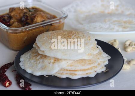 Reispfannkuchen und Trichter. Zwei Arten von Frühstücksgerichten mit rotem Reis zusammen mit Hühnerfleisch, das mit hausgemahlenem Masala zubereitet wird. Aufgenommen auf weißem Hintergrund Stockfoto