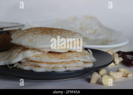 Reispfannkuchen und Trichter. Zwei Arten von Frühstücksgerichten mit rotem Reis zusammen mit Hühnerfleisch, das mit hausgemahlenem Masala zubereitet wird. Aufgenommen auf weißem Hintergrund Stockfoto