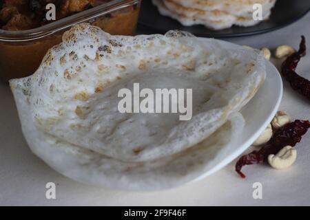 Trichter und Reispfannkuchen. Zwei Arten von Frühstücksgerichten mit rotem Reis zusammen mit Hühnerfleisch, das mit hausgemahlenem Masala zubereitet wird. Aufgenommen auf weißem Hintergrund. Stockfoto