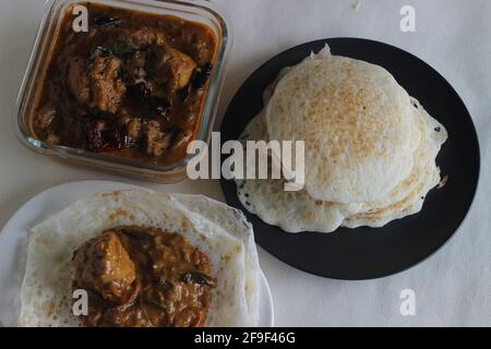 Trichter und Reispfannkuchen. Zwei Arten von Frühstücksgerichten mit rotem Reis zusammen mit Hühnerfleisch, das mit hausgemahlenem Masala zubereitet wird. Aufgenommen auf weißem Hintergrund. Stockfoto