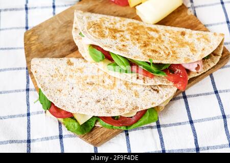 Piadina Romagnola mit Mozzarella-Käse, Tomaten, Schinken und Rucola-Salat auf einem Schneidebrett. Italienisches Fladenbrot oder offenes Sandwich. Selektiver Fokus. Stockfoto