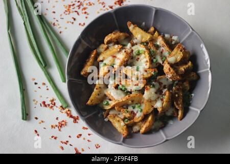 Kitschige Kartoffelkeile, die aus gebratenen Kartoffelkeilen in Backluft hergestellt wurden, nachdem sie mit zerfetzten Mozzarella, Chilischoten und gehackten grünen Zwiebeln bestreut wurden. Aufnahme Stockfoto