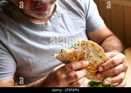 Mann, der Piadina Romagnola mit Mozzarella-Käse, Tomaten, Schinken und Rucola isst. Italienisches Fladenbrot oder offenes Sandwich. Selektiver Fokus. Stockfoto