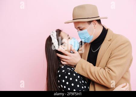 Liebevolles junges Paar küsst sich, während es medizinische Masken trägt. Stockfoto