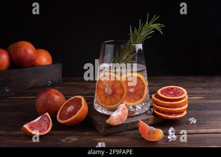 Glas mit funktionellem Wasser mit blutroangen Scheiben und Rosmarin auf dunklem Holzboden, Orangensaft, Nahaufnahme. Stockfoto