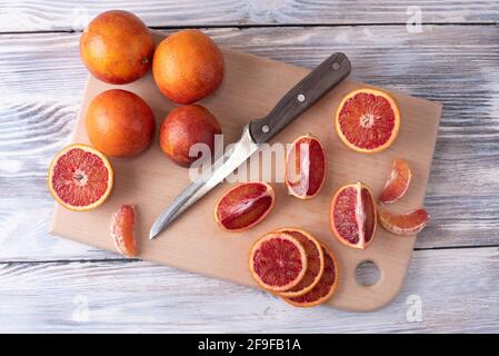 Blutroorangene Scheiben auf Schneidebrett mit ganzen Zitrusfrüchten auf weißem Holzhintergrund, gesunde Ernährung, Nahaufnahme. Stockfoto