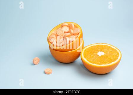 Halb Orange und mit Vitamin C-Tabletten auf blauem Hintergrund schälen, Nahaufnahme. Vitamin C Pillen als Alternative zu Zitrusfrüchten. Konzept des Immunverstärkers Stockfoto