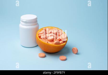 Weiße Flasche und orangefarbene Vitamin C-Tabletten mit einer halben Orange auf blauem Hintergrund, Mockup. Konzept des Immunverstärkers. Stockfoto