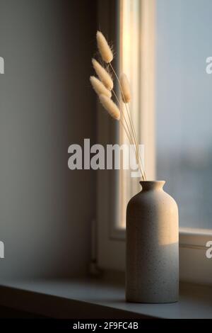 Vase mit flauschigen, getrockneten Blumen auf der Fensterbank bei Sonnenuntergang. Einrichtung im skandinavischen Stil. Stockfoto