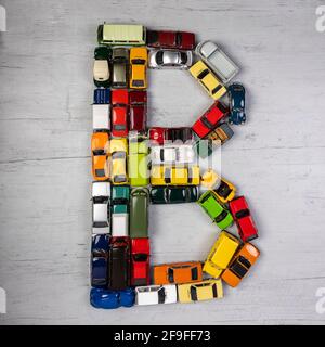 Der Buchstabe B, gebildet mit Spielzeugautos, auf einem grauen hölzernen Brett Stockfoto