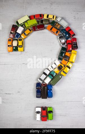 Fragezeichen, gebildet mit Spielzeugautos, auf einem grauen Holzbrett Stockfoto