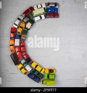Der Buchstabe C, gebildet mit Spielzeugautos, auf einem grauen hölzernen Brett Stockfoto