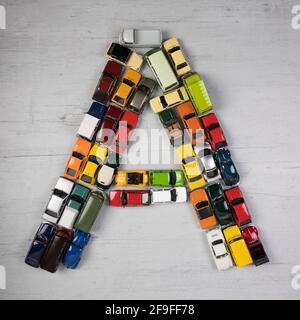 Der Buchstabe A, gebildet mit Spielzeugautos, auf einem grauen hölzernen Brett Stockfoto