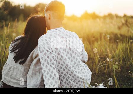 Stilvolles, schönes Paar, das den Sonnenuntergang genießt und sich auf der Sommerwiese bei warmem, sonnigem Licht auf der Decke entspannt. Urlaub und Picknick. Junge Boho-Familie Stockfoto