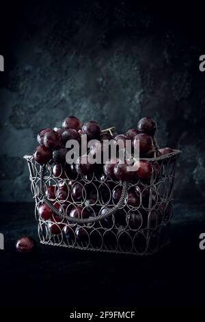 Nahaufnahme eines Bukets roter Trauben in einem Drahtgeweben kleinen Korb, schwarzer Hintergrund. Stockfoto