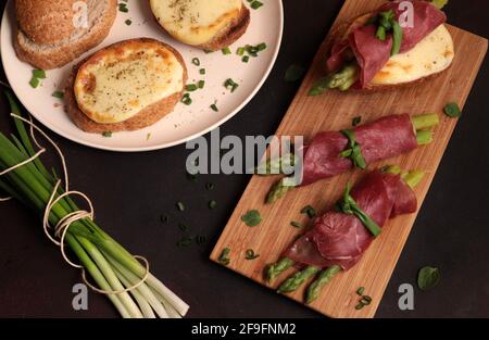 Bresaola und Spargelbrötchen mit Käse und geröstetem Brot auf dunklem Hintergrund. Gesunde Ernährung. Blick von oben. Stockfoto