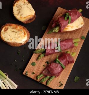 Bresaola und Spargelbrötchen mit Käse und geröstetem Brot auf dunklem Hintergrund. Gesunde Ernährung. Blick von oben. Stockfoto