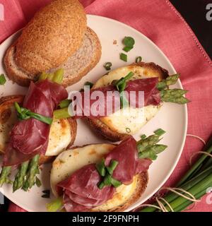 Bresaola und Spargelbrötchen mit Käse und geröstetem Brot auf dunklem Hintergrund. Gesunde Ernährung. Blick von oben. Stockfoto